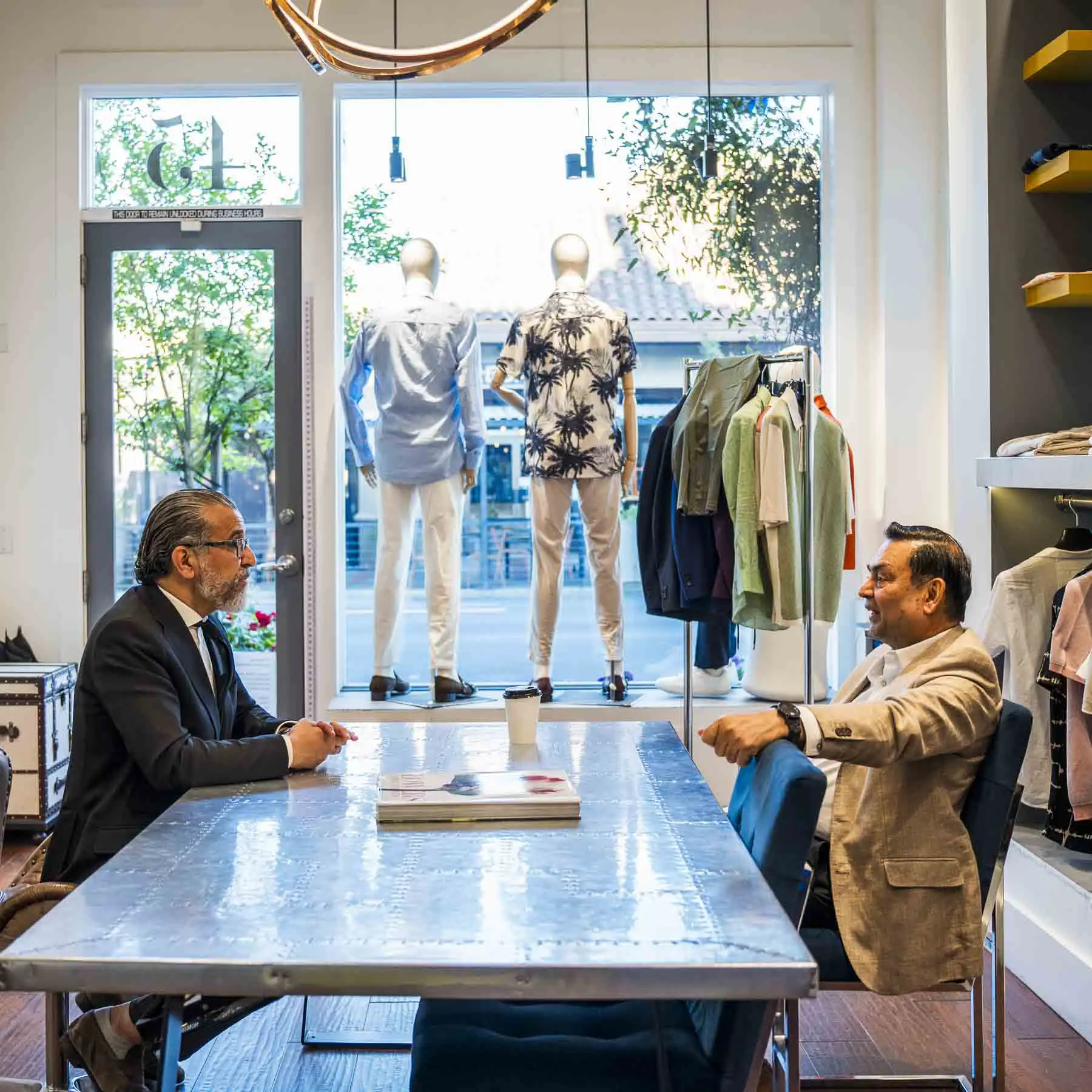 Two men sitting at a table in front of mannequins.